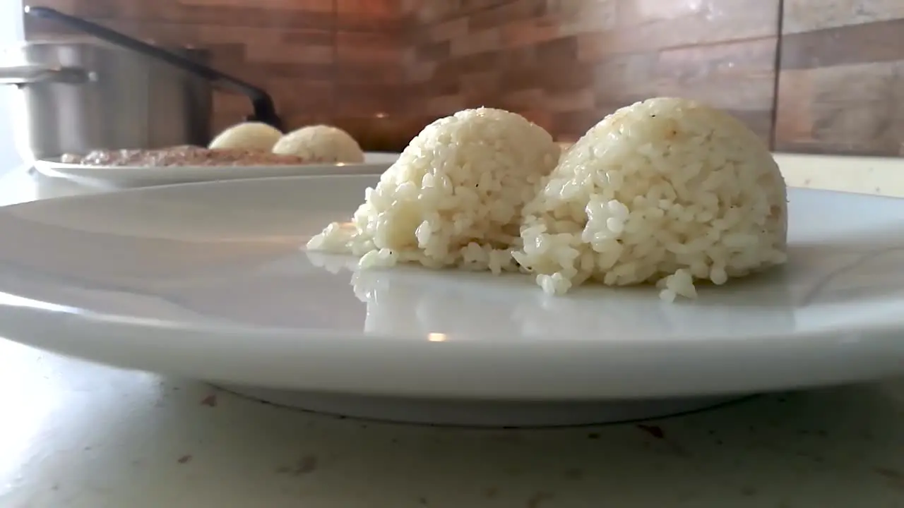 Chef plating balls of steaming hot white rice on a round plate with a plastic ladle