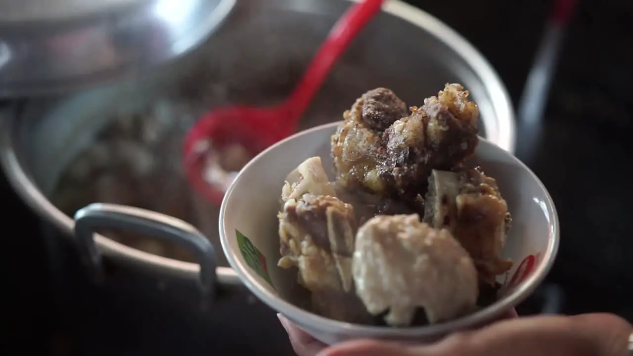 Hands take meatballs from pot to bowl containing beef bones