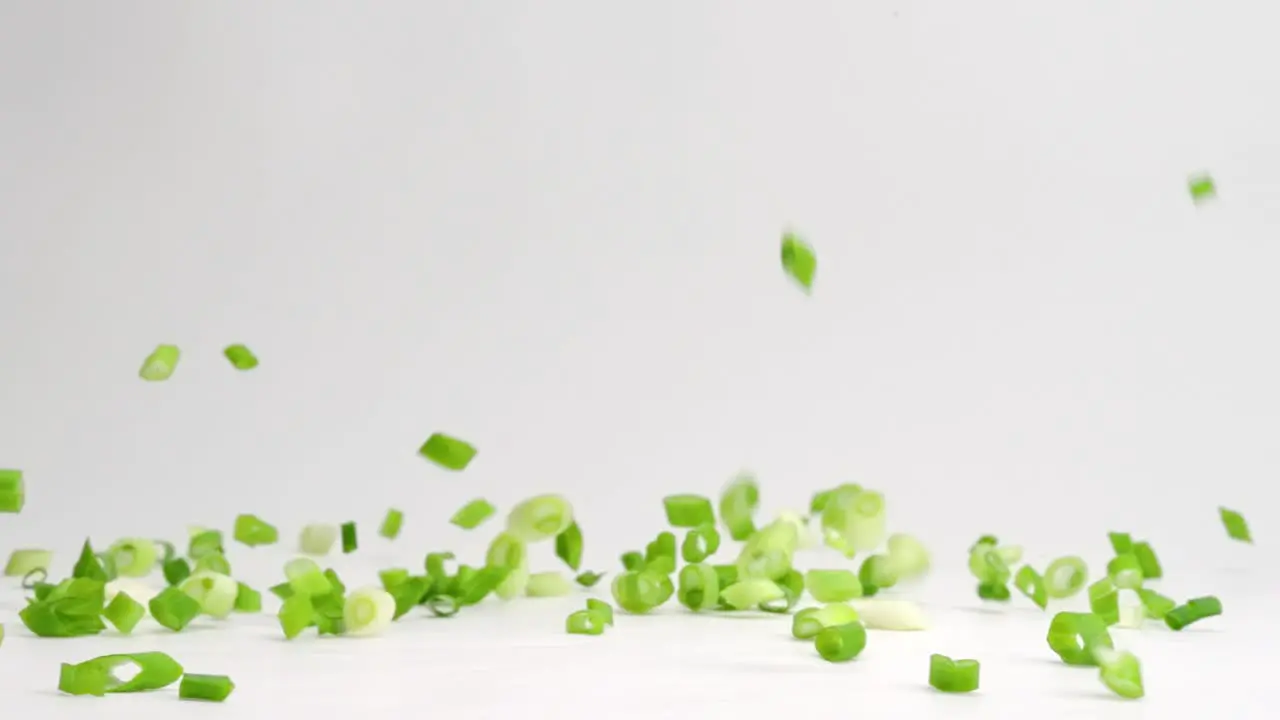 Diced and chopped green onion pieces falling and bouncing onto white table top in slow motion