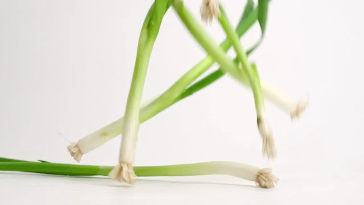 Green scallion onions landing and bouncing on white table top in slow motion