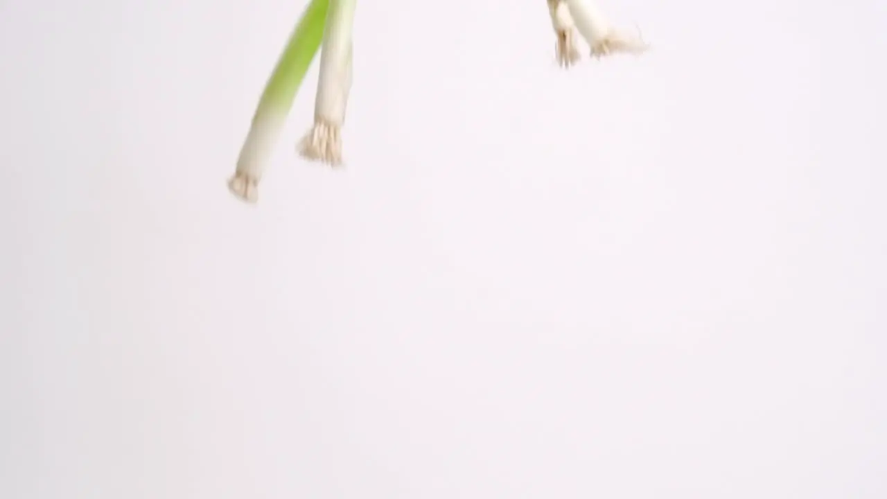 Whole green onions raining down on white backdrop in slow motion