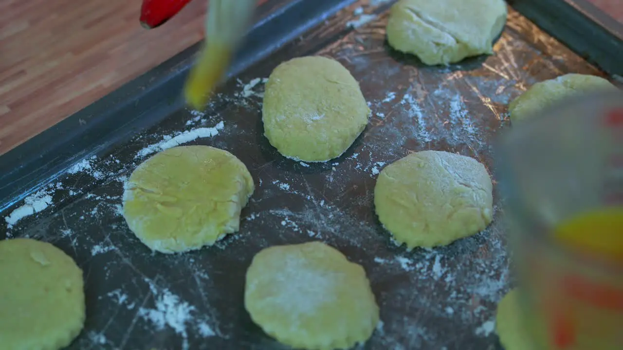 Brushing the tops of formed scones on a baking tray female hand