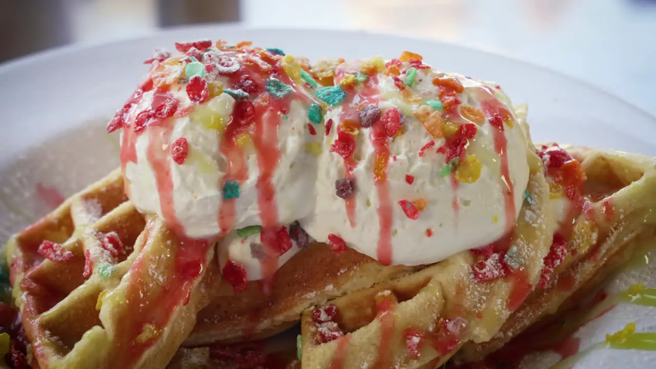 Confetti Belgian waffles filled with fruity pebbles rice cereal and topped with ice cream and syrup close up 4K