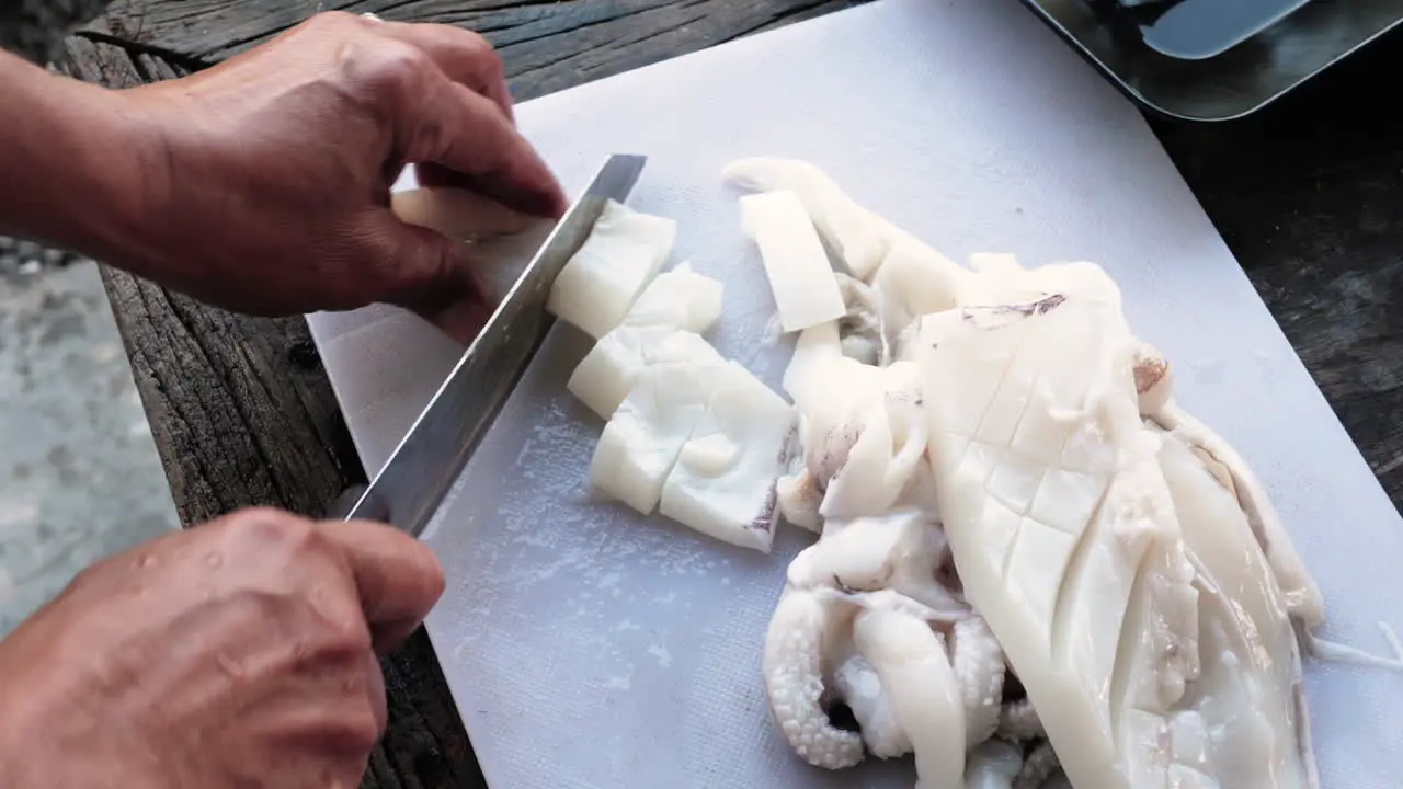 Person cuts a squid fillet with a knife into calamari rings white cutting board