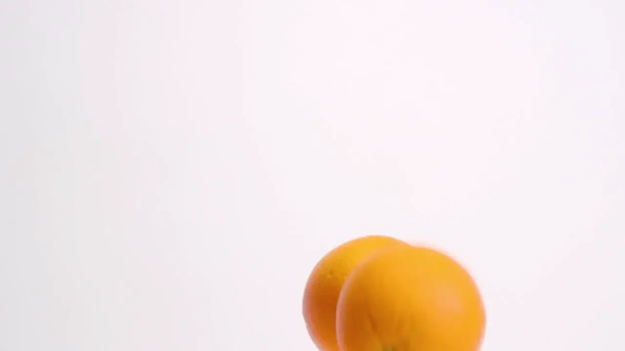 Whole oranges falling on white studio backdrop in 4k slow motion