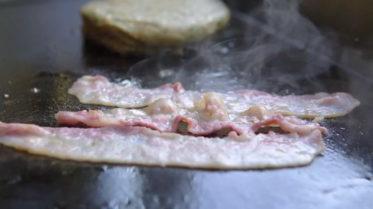 cooking slices of bacon on a grill next to a burger in fast food restaurant slow motion