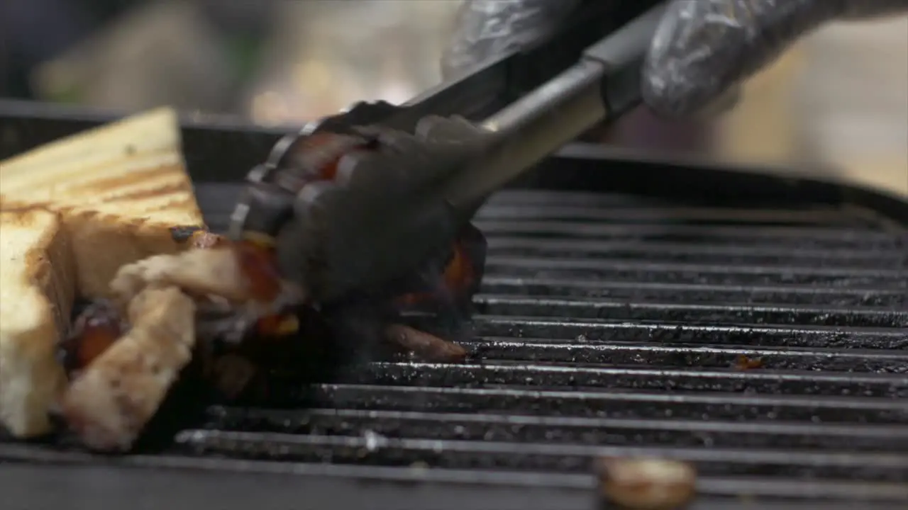 Pieces of pork meat being tossed on grill and grilled toast being removed from grill filmed as close up shot in handheld style