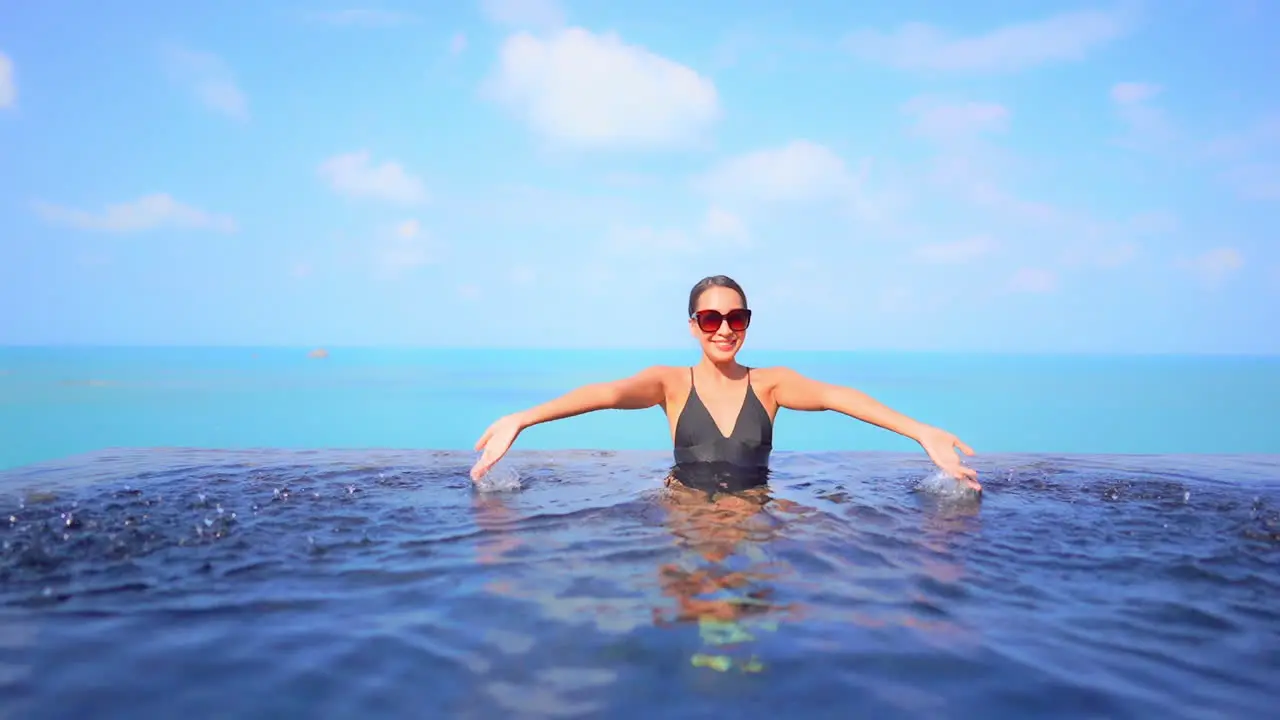 With the ocean as a backdrop a pretty young woman playfully splashes water in the swimming pool