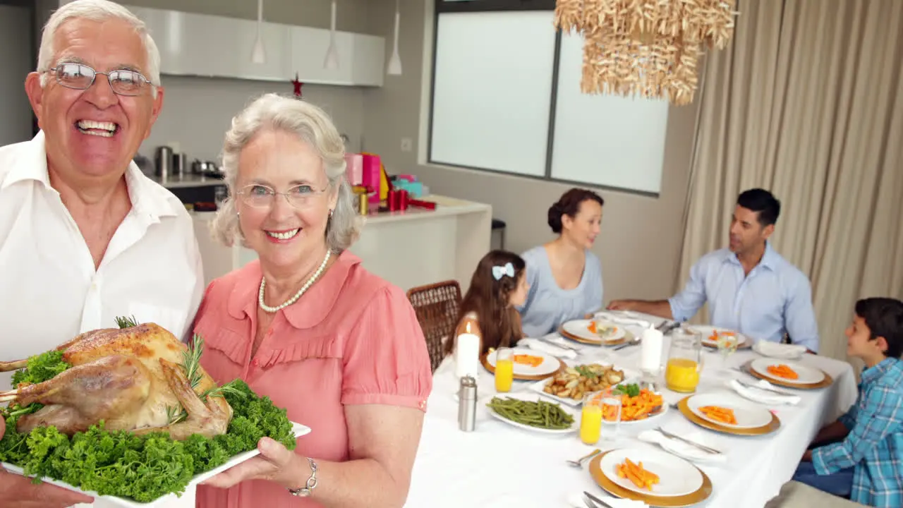 Proud grandparents holding roast chicken with family behind them