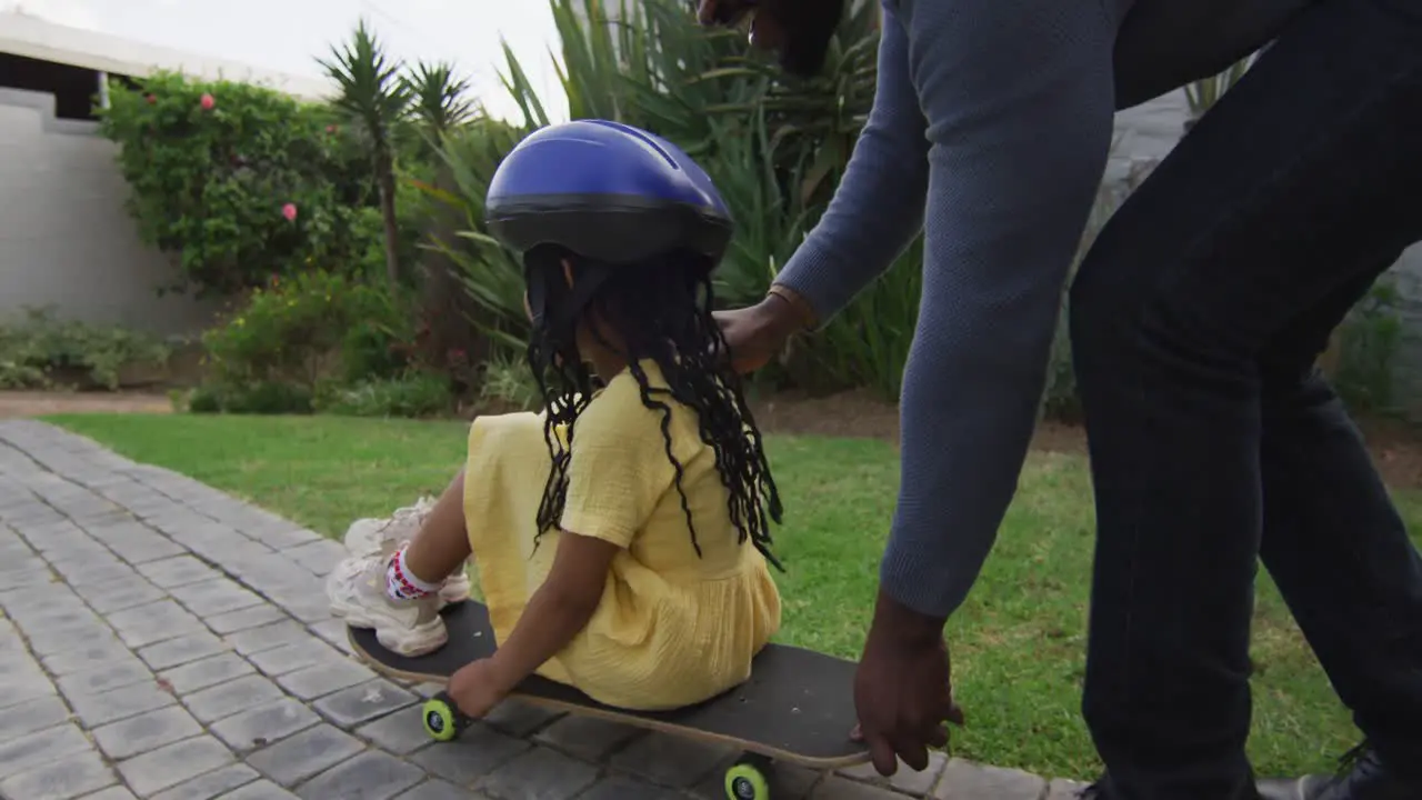 Happy african american father playing with daughter on skateboard in backyard