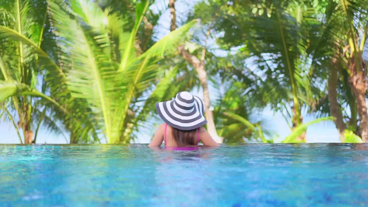 Back view of woman with large hat and pink swimsuit in pool edge