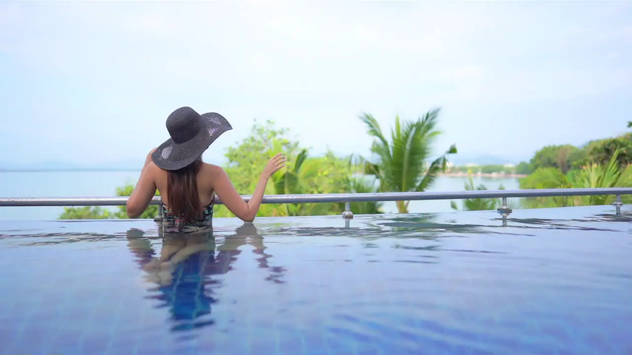 A young woman looks out on the tropical landscape and ocean horizon from the edge of a resort swimming pool