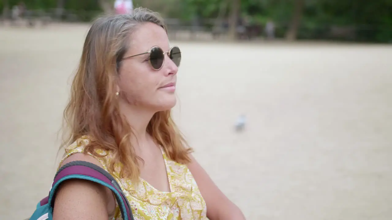 Woman in sunglasses spending the weekend outdoors sitting and looking around in the park close up