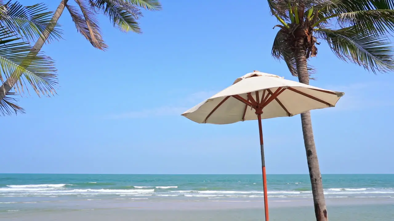 One white sun umbrellas on tropical exotic beach with palm trees and sea in background