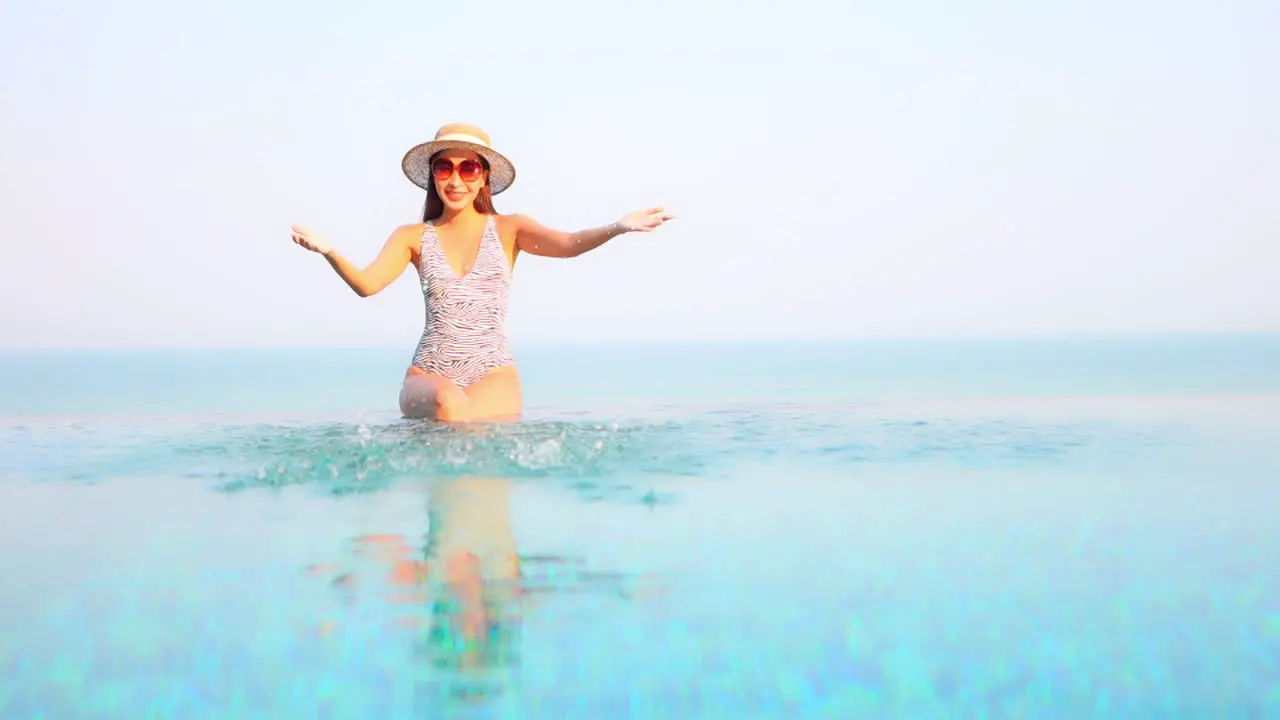 Asian woman splash water with hands in rooftop infinity pool