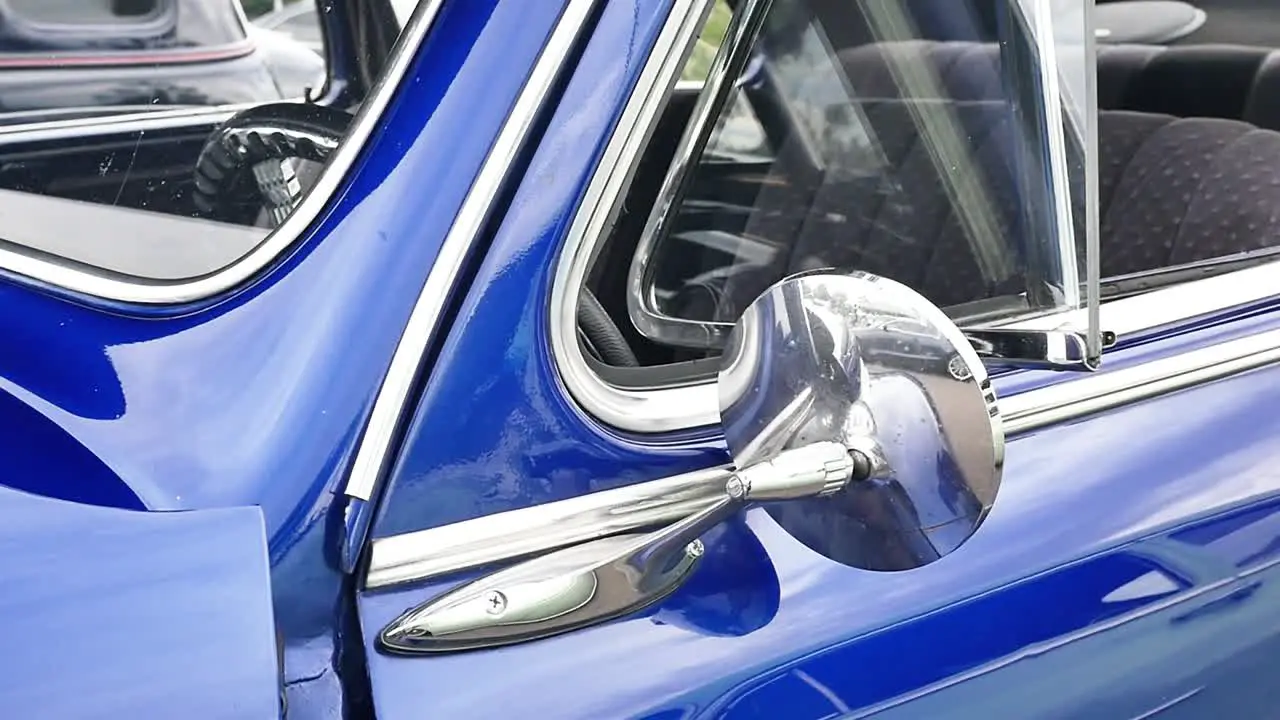 Slow push-in on reflective side-view mirror on a blue classic car with the windows down