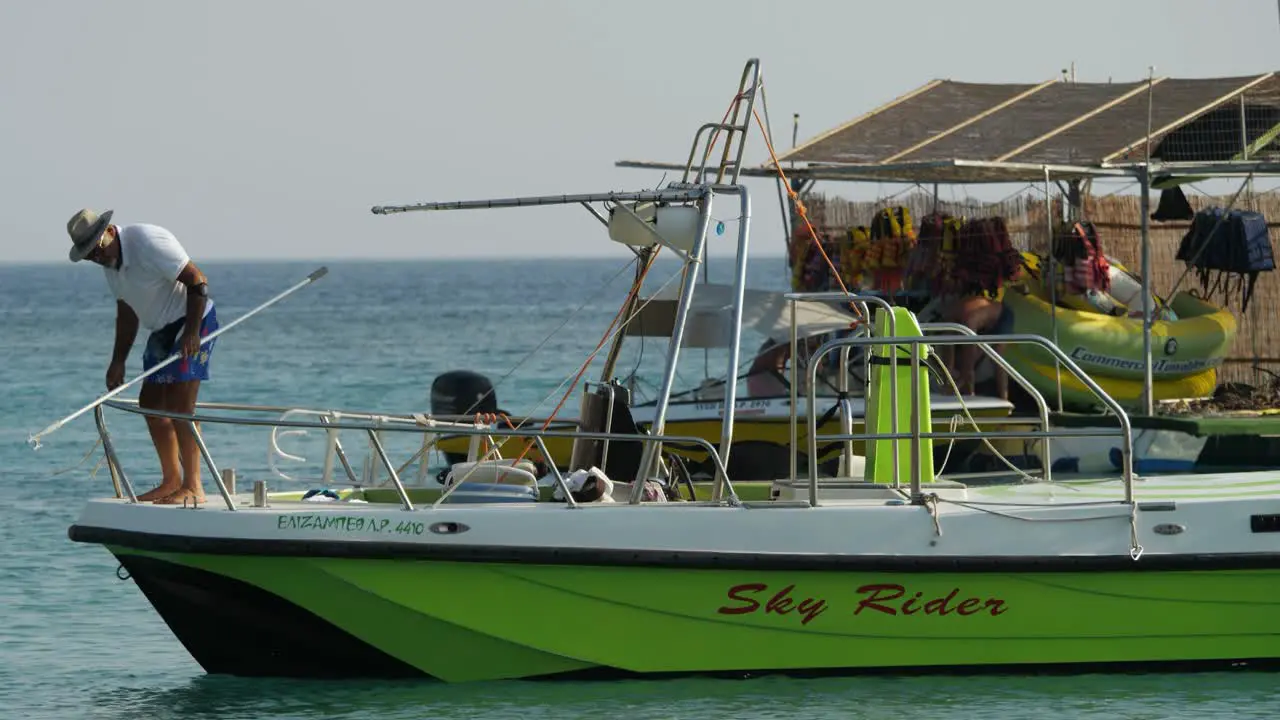 Man on a green boat looking for something in the water at Kolymbia Harbour