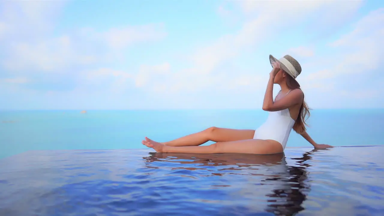 An attractive young woman appears to be floating in midair along the water's edge of an infinity-edge pool ocean background