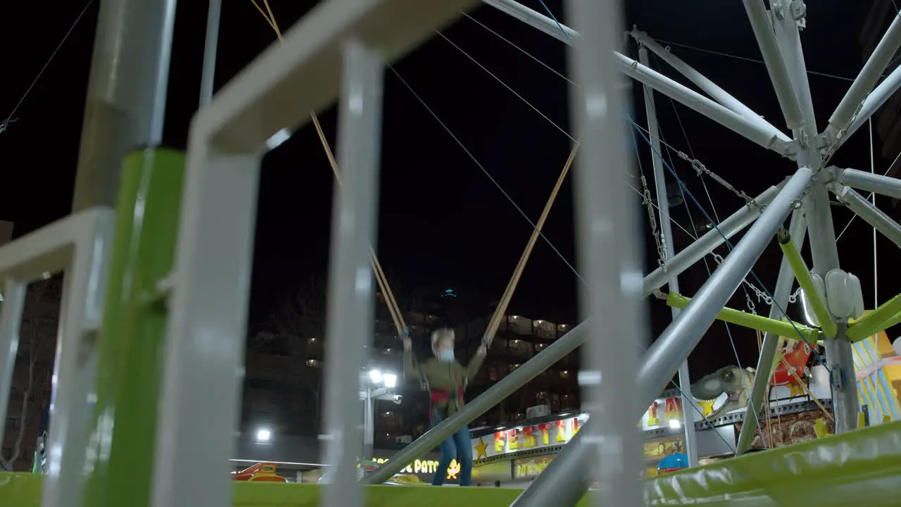 Boy jumping on bungee trampoline in funfair at night