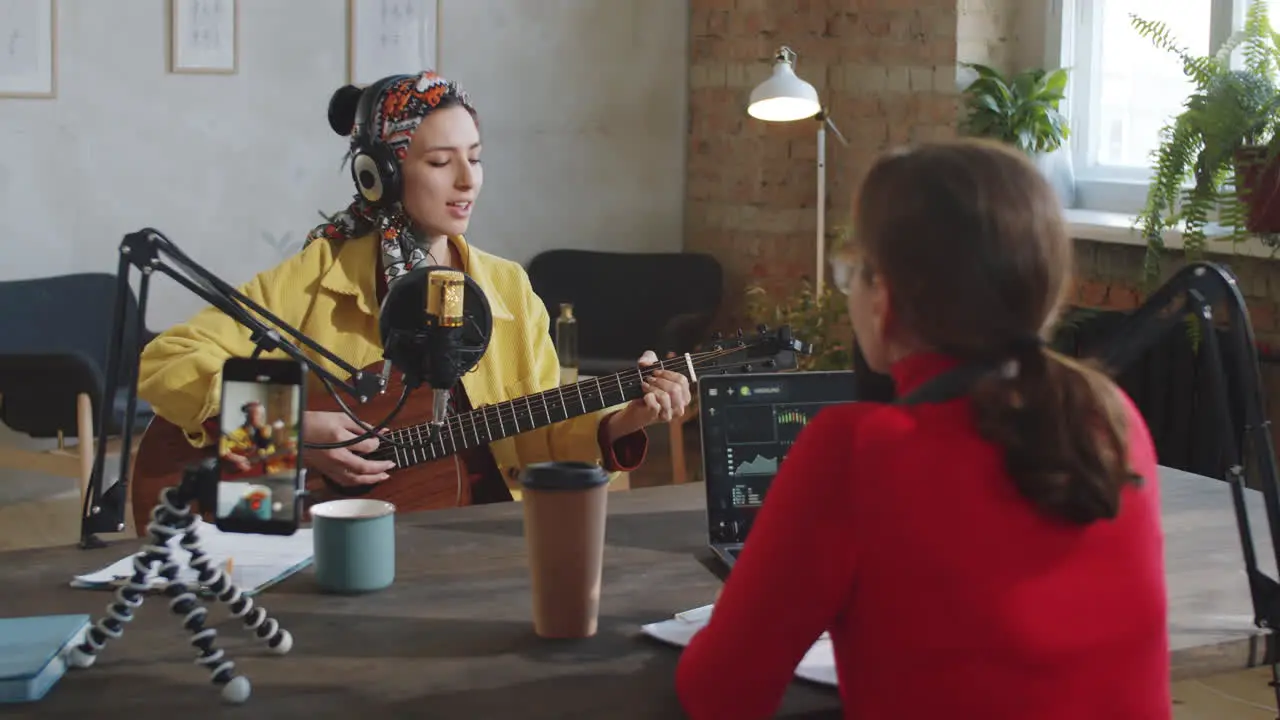 Woman Playing Guitar and Singing while Recording Podcast