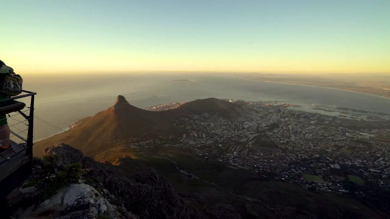 A family of tourists poses for a photo from a lookout deck on top of Table Mountain while the camera pans across to reveal the beautiful views of Cape Town