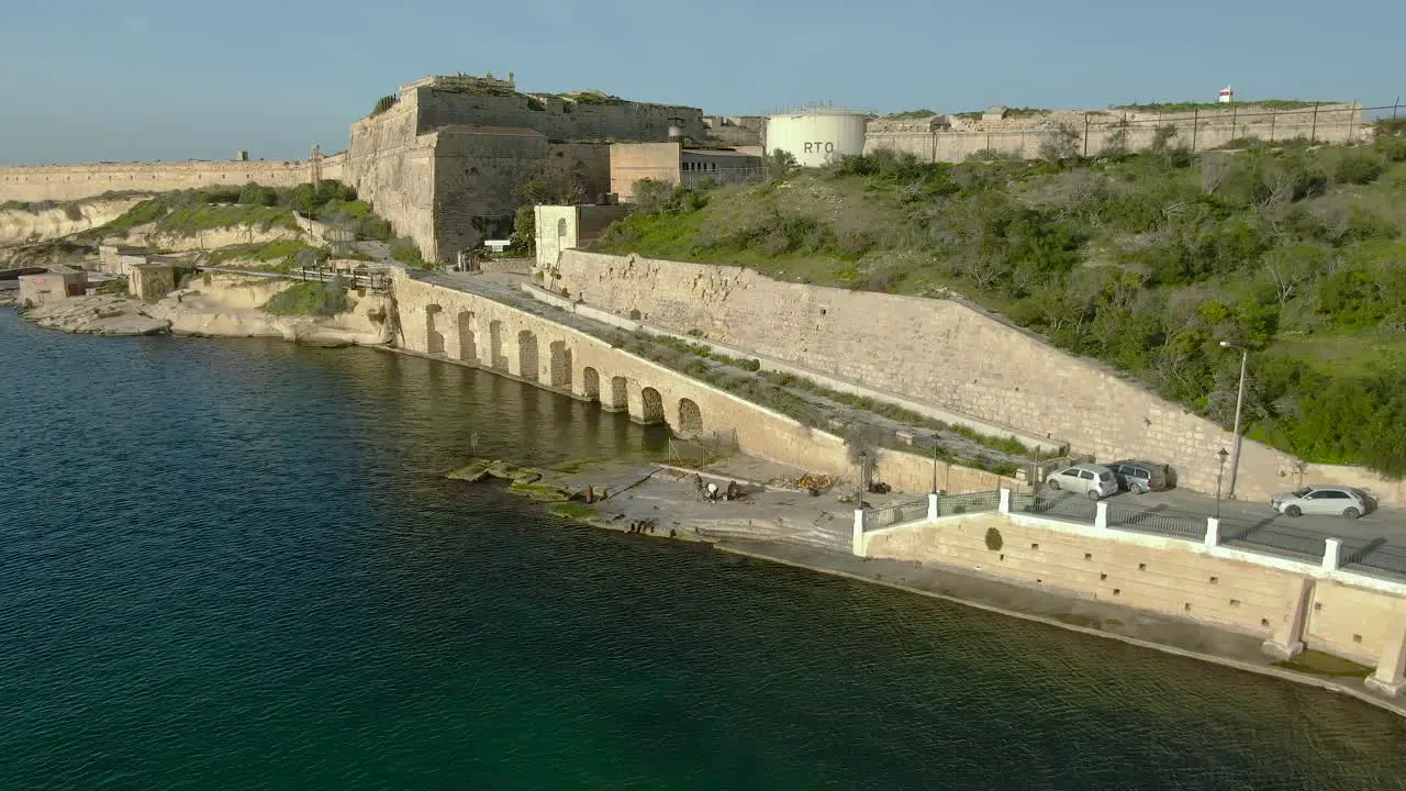 Dronie Aerial Shot over the sea away from a crane and an old city and a fort