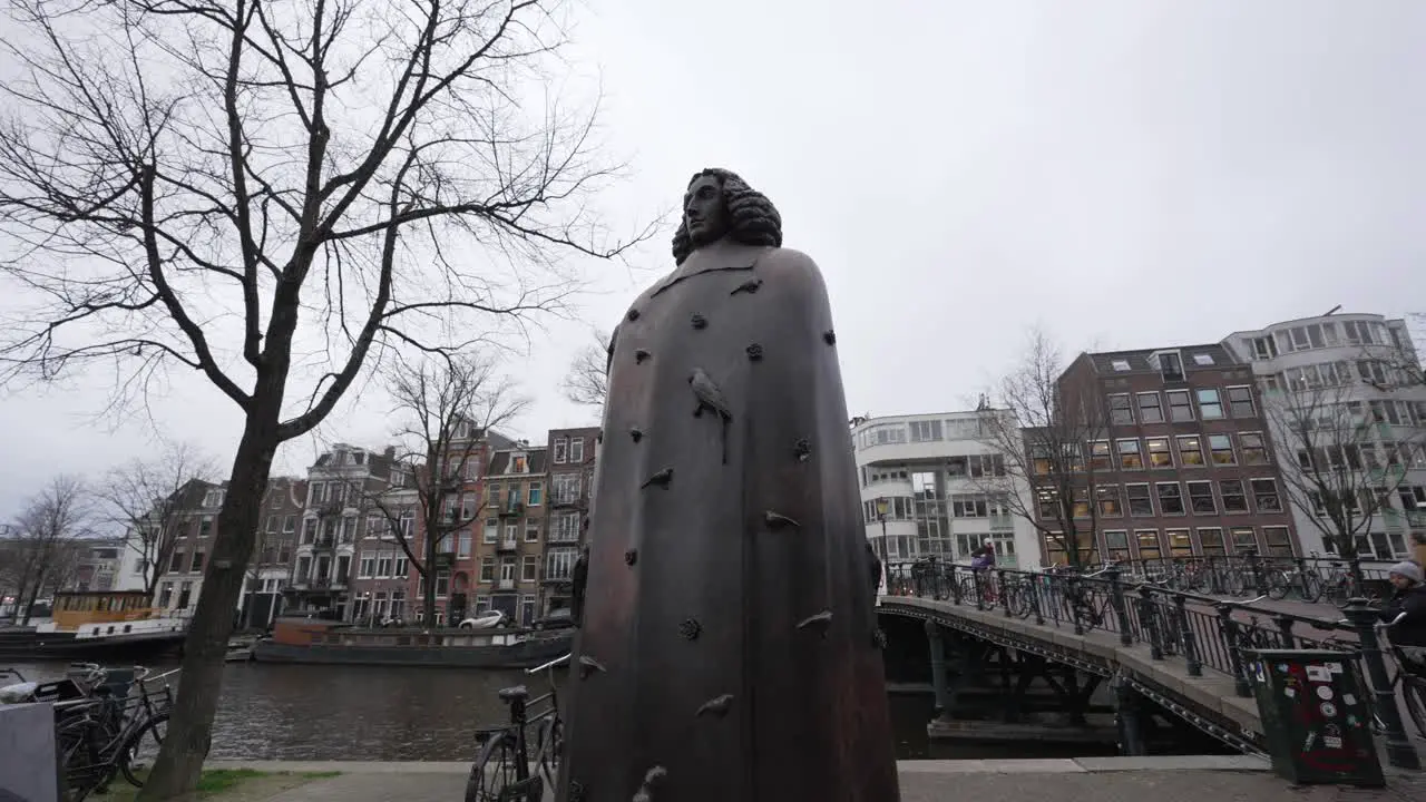 Low angle shot of statue in Amsterdam with pedestrians crossing bridge over the canal