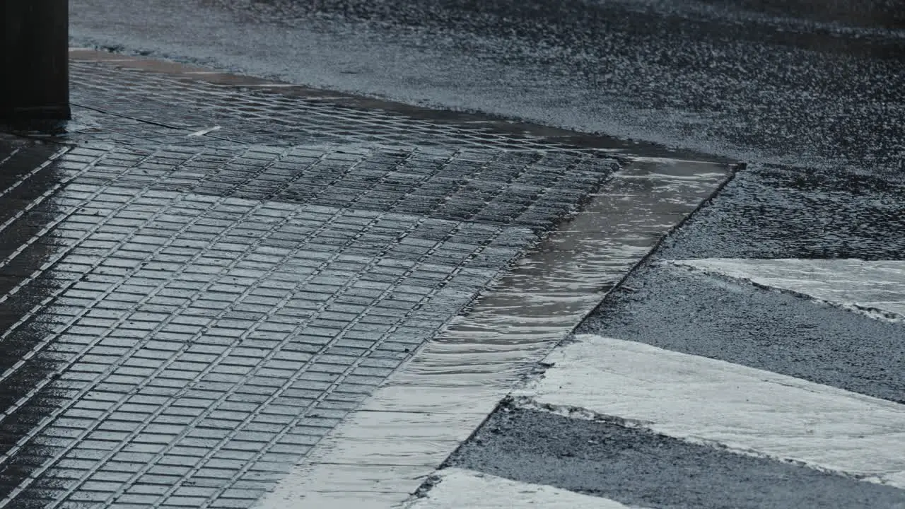 Close up of water flowing through drainage system in a urban city as it rains and cars pass by