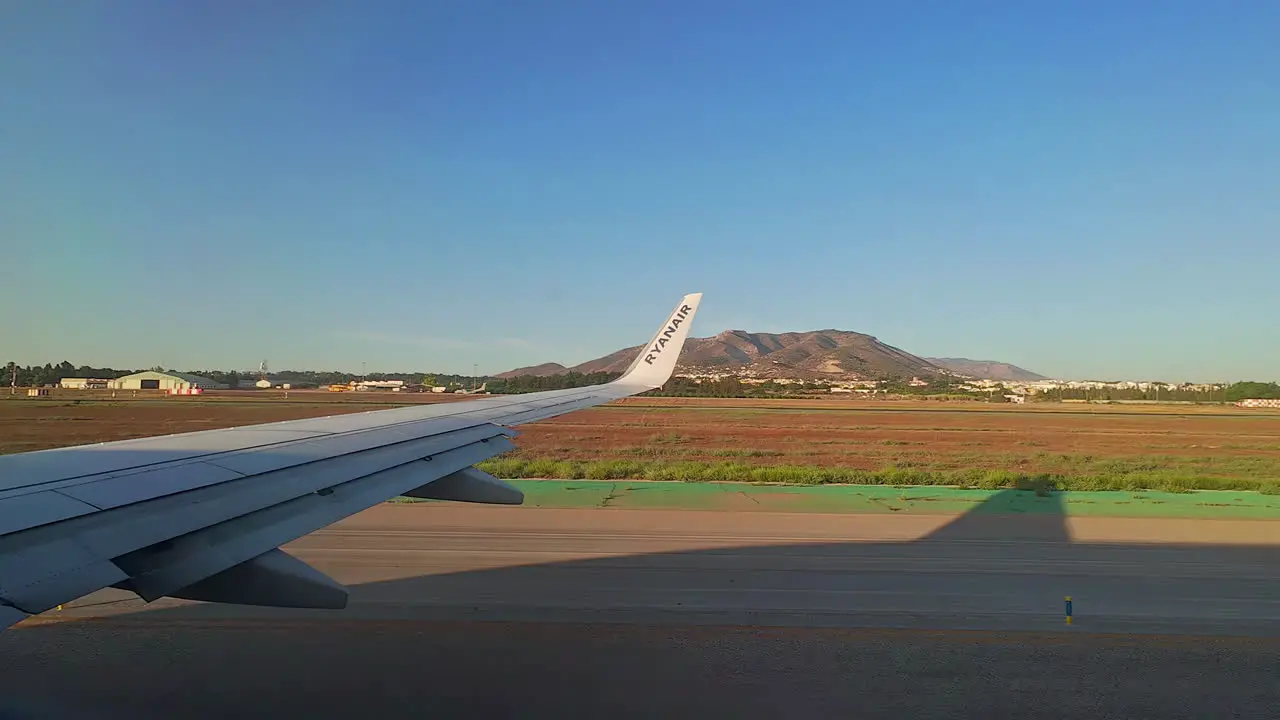 View out of aeroplane window showing wing and mountainous landscape surrounding airport runway