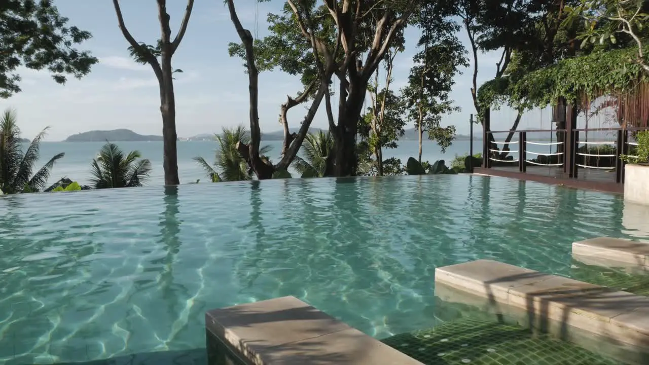 infinite swimming pool with background of natural sea and mountain view with some tree