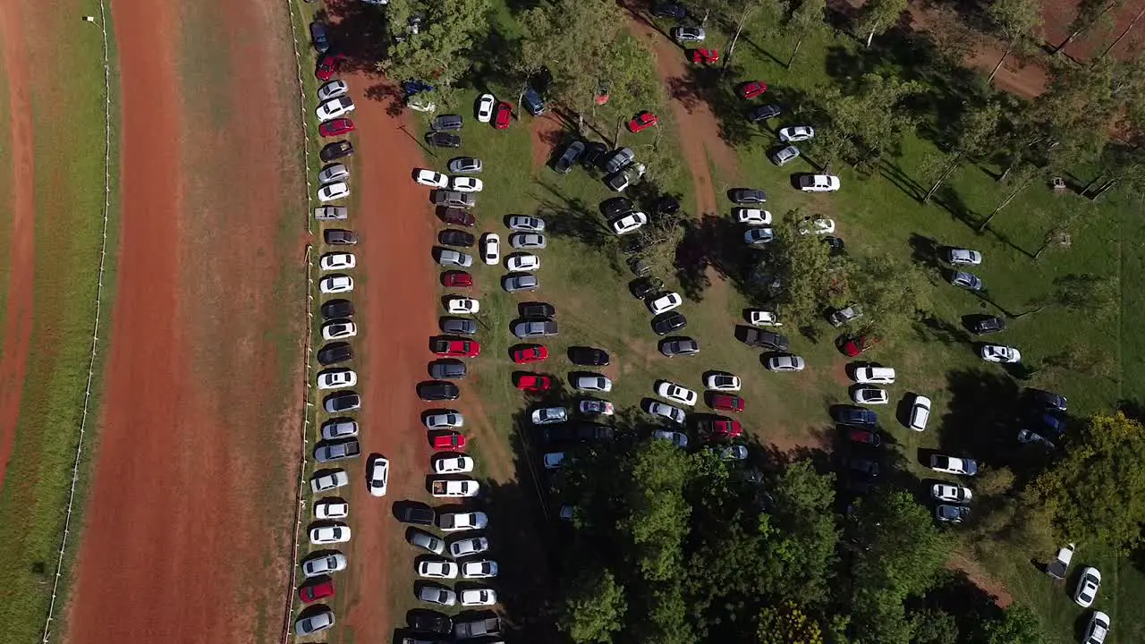 Drone look-down on cars parked in wooded area revealing traffic on nearby road pan left to right