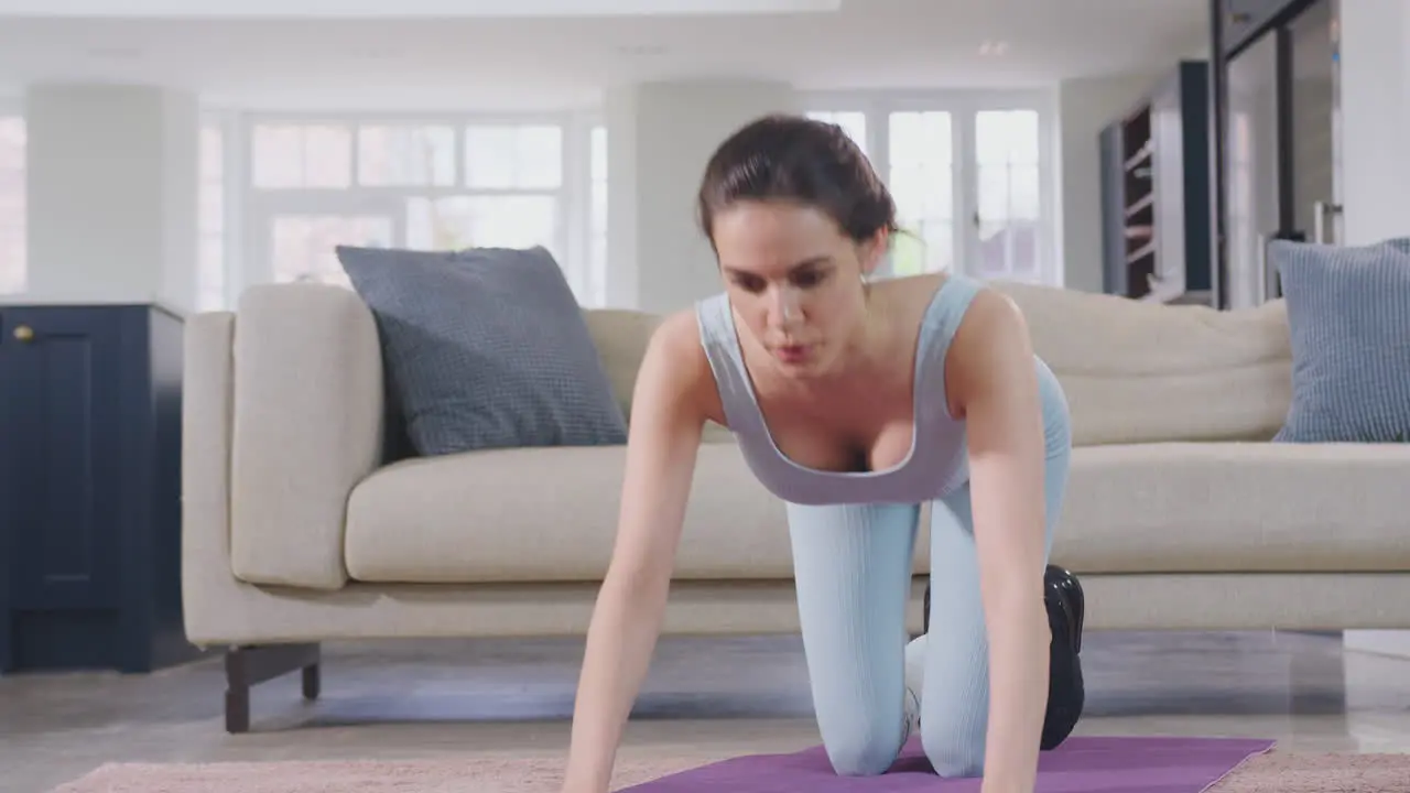 Woman in fitness clothing at home in lounge doing stretches and exercising on mat shot in slow motion