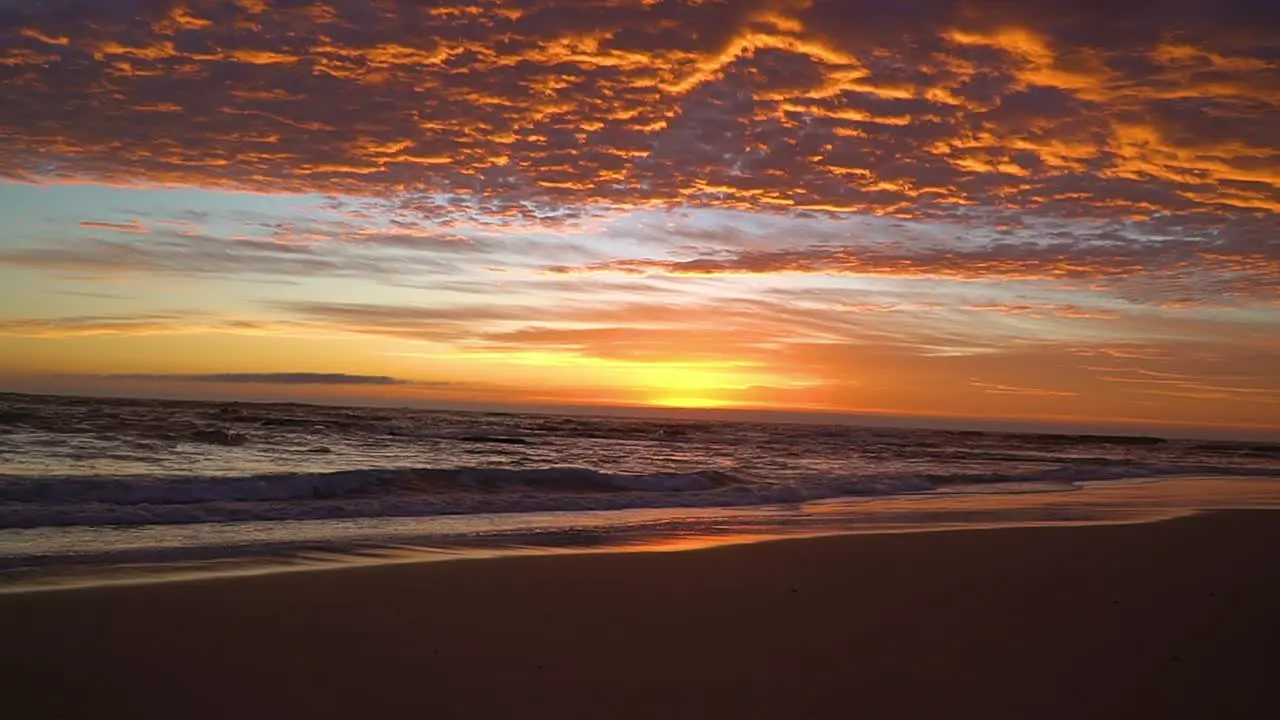 slow motion cinematic sunrise of fire sky with foamy ocean waves lapping on the shore golden reflection beach