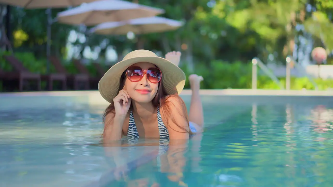 A happy young Asian woman relaxing in a swimming pool at a hotel resort