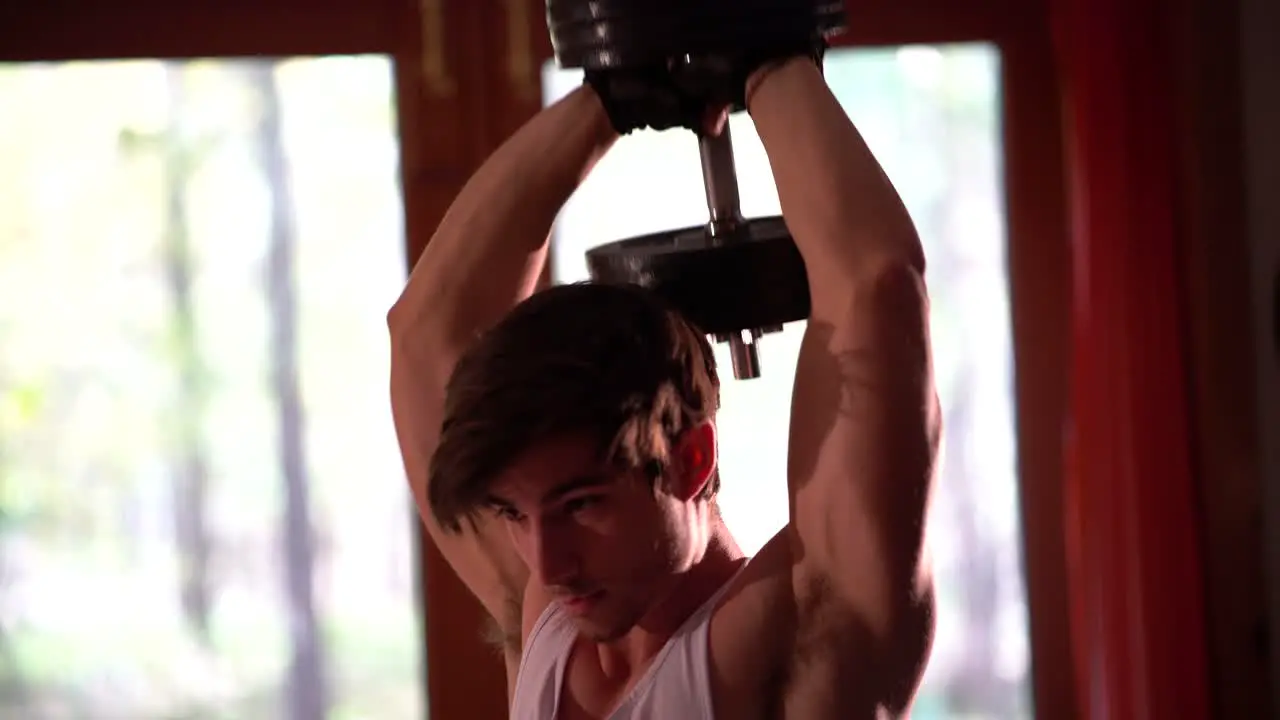 Tight shot of a teen bodybuilder doing a military press or tricep extension behind his head with a heavy group of weights