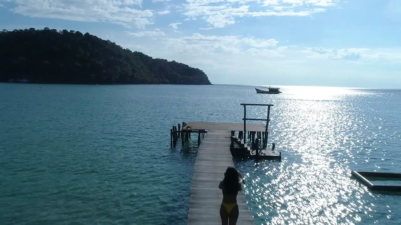 Silhouette of a fit girl walking alone on a pier in the ocean on a tropical island koh kood Thailand