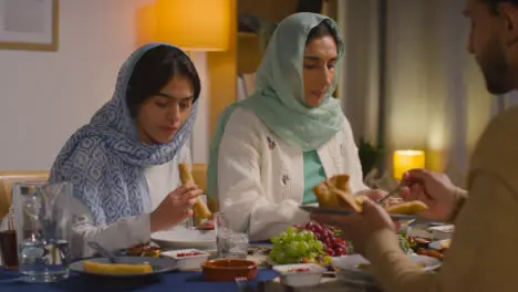 Muslim Muslim Family Sitting Around Table At Home Eating Meal Together 1