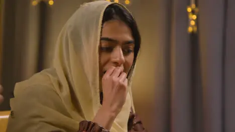 Young Muslim Woman Sitting Around Table At Home Drinking Water And Eating Meal Celebrating Eid