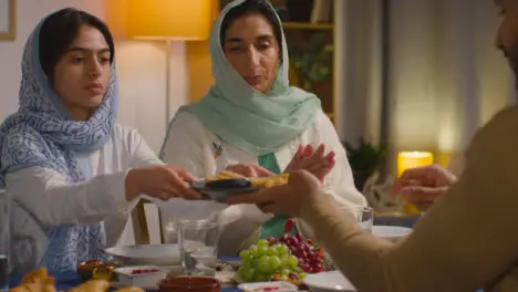 Muslim Muslim Family Sitting Around Table At Home Eating Meal Together