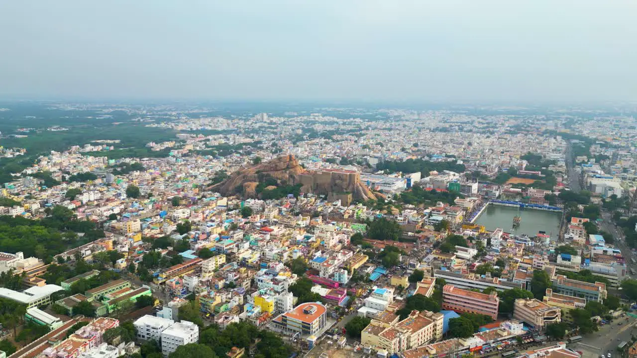 Malaikottai rock fort in middle of Tiruchirappalli city's dense urban buildings aerial panoramic dolly