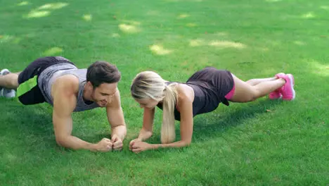 Athlete man and woman training together plank exercise on lawn in summer park