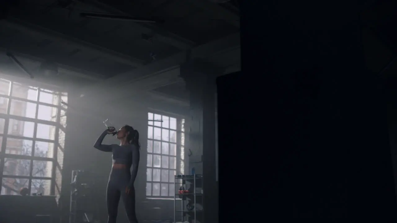 Woman standing in gym with water bottle Girl drinking water from bottle