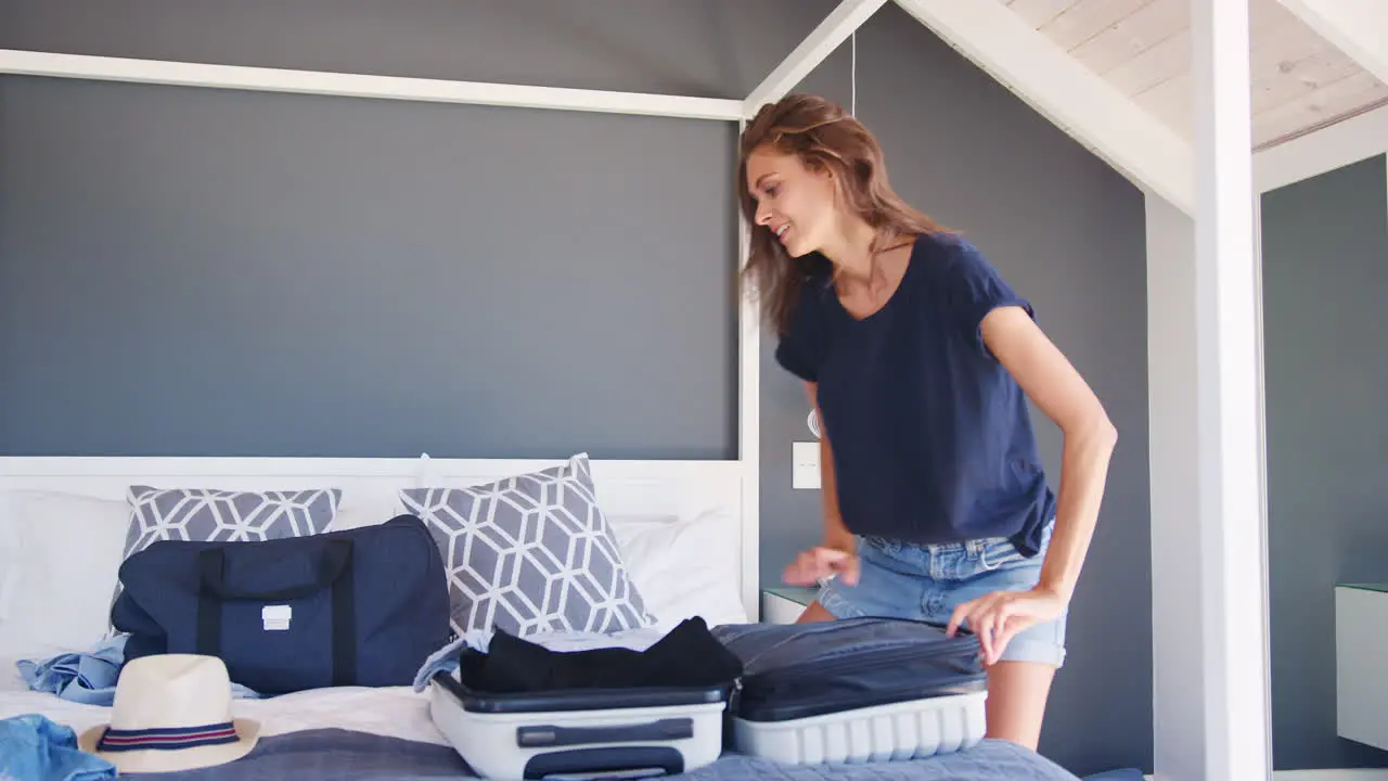 Woman Trying To Close Full Holiday Suitcase In Bedroom