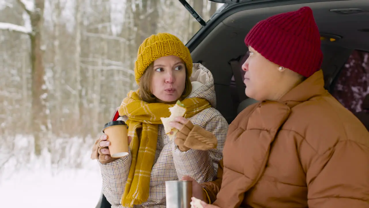 Happy Couple Drinking And Eating Sandwich While Sitting In Car Boot On A Cold Winter Day