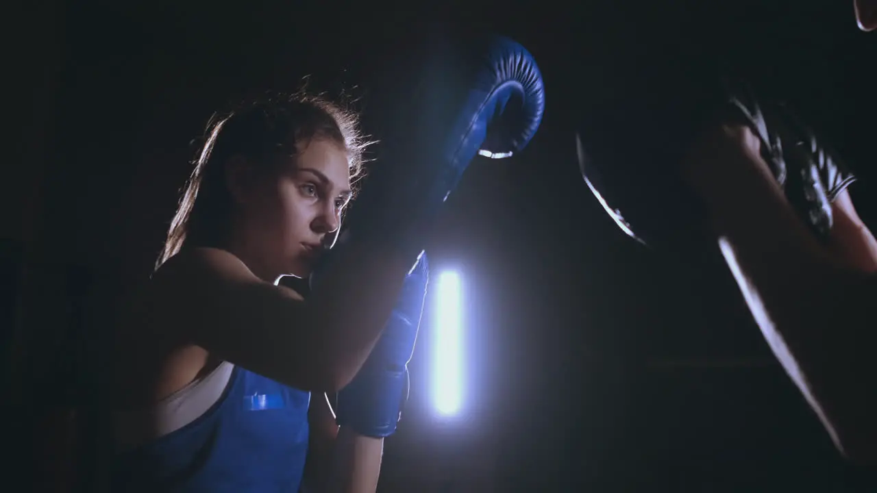 Medium shot of beautiful fitness woman boxer treneruemsya strike speed focus mitts with a coach in a Boxing club slow motion