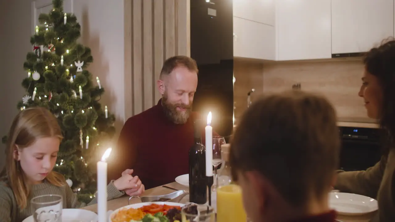 Couple And Their Children Pray And Bless The Table Before Christmas Family Dinner 2