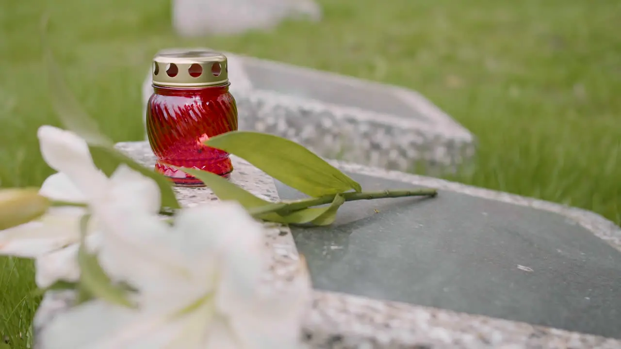 Vista De Cerca De Un Hombre Irreconocible Con Traje Negro Arrodillado Y Poniendo Flores Y Una Vela En Una Lápida En Un Cementerio