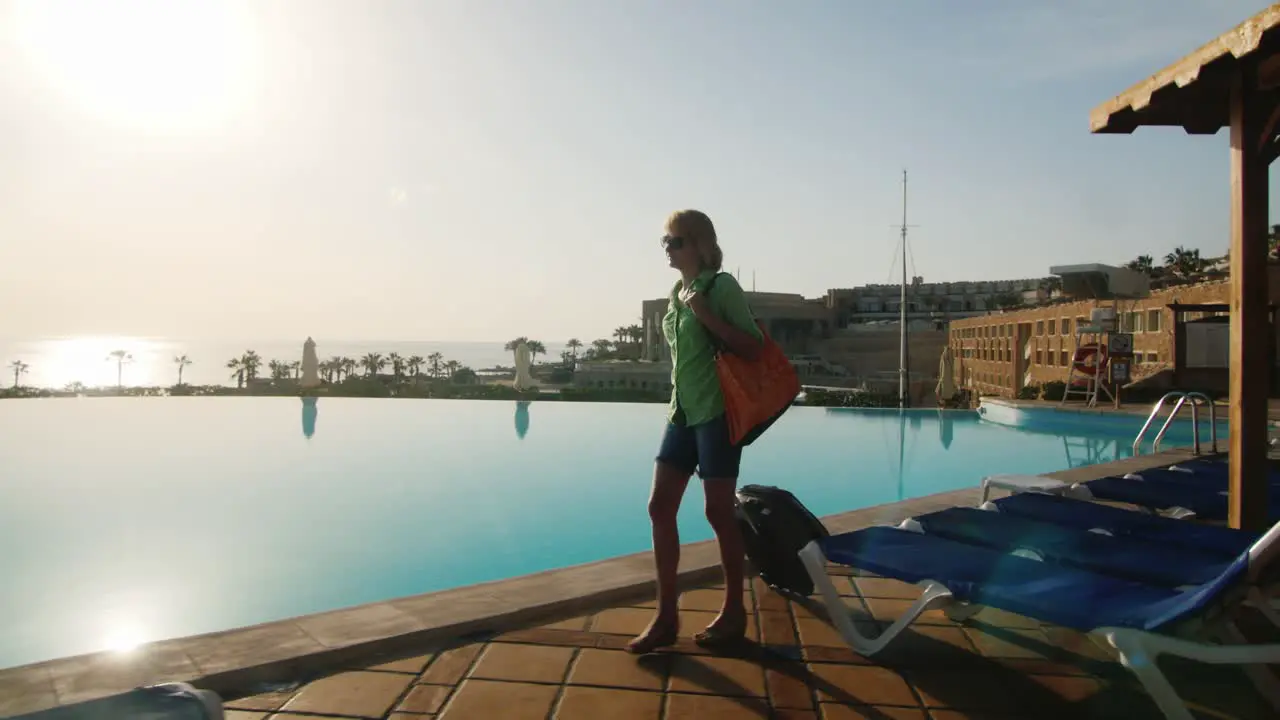 Steadicam Shot Of Woman With Travel Bag Walking On Recreation Area Along The Pool