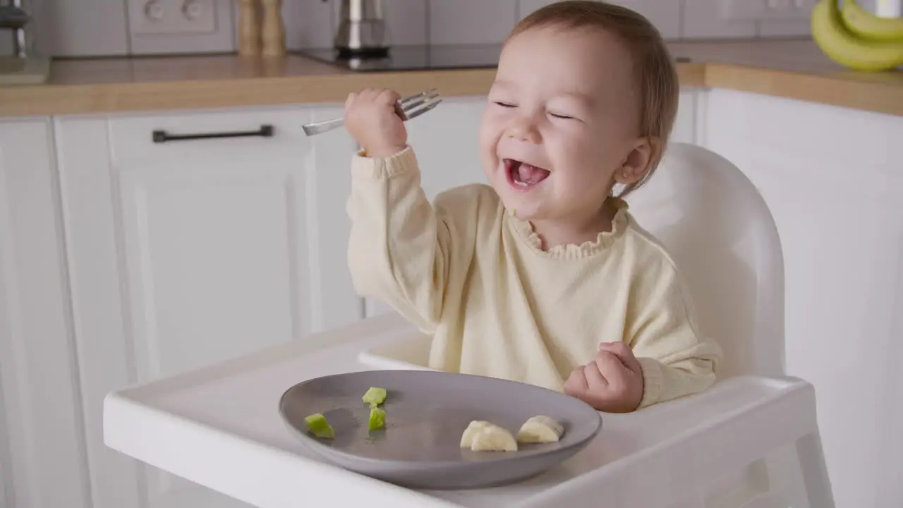 Süßes Kleines Mädchen Das Avocadoscheibe Mit Gabel Isst Während Es In Einem Hochstuhl In Der Küche Sitzt