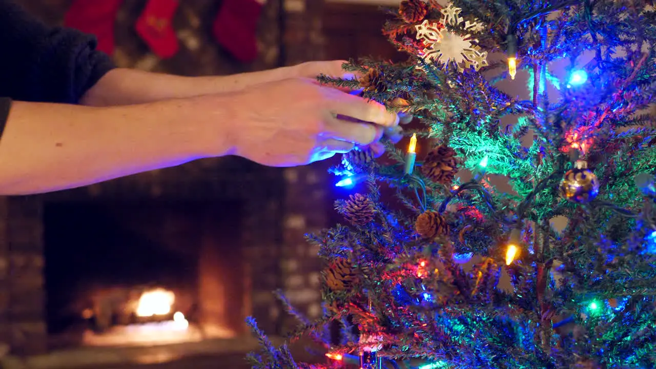 Close up on a family decorating a christmas tree together with lights and ornaments and stockings over the fireplace during the holidays